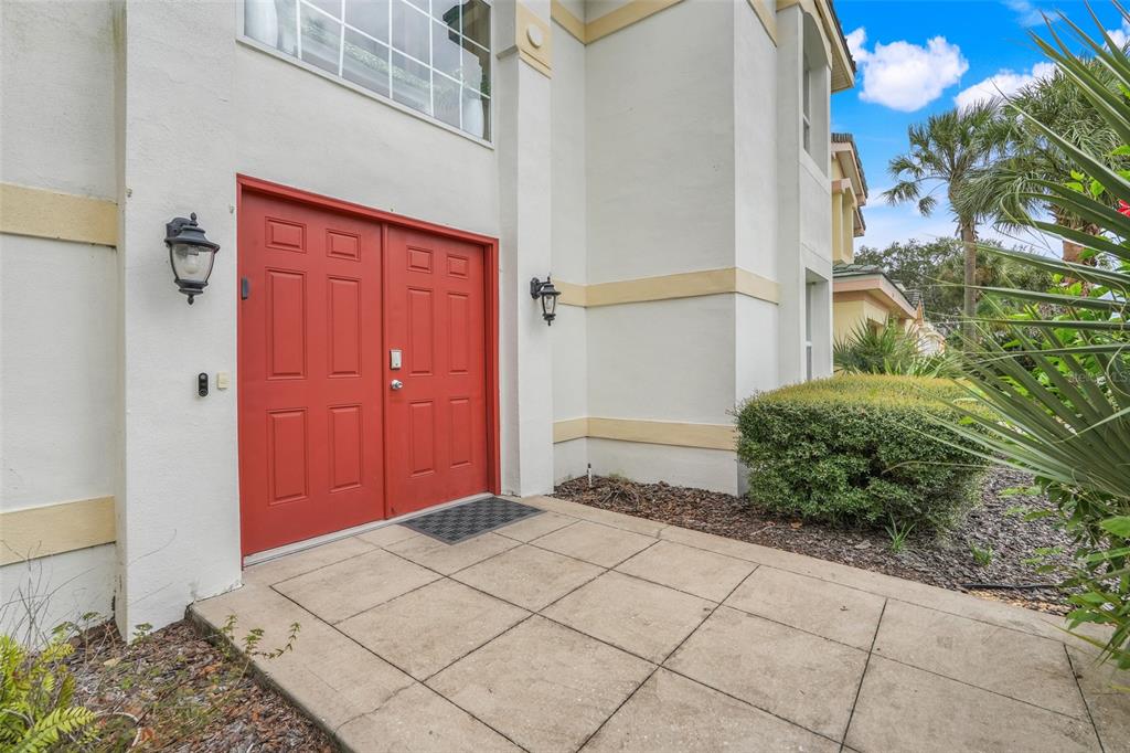 A red double front door sits on a concrete patio next to a green bush — 8807 CRAYSON COURT, KISSIMMEE, FL