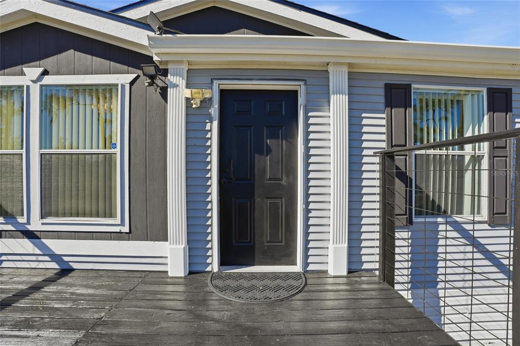 A black front door with white columns sits on a wooden deck of a house — 3844 KAISER AVENUE, ST CLOUD, FL