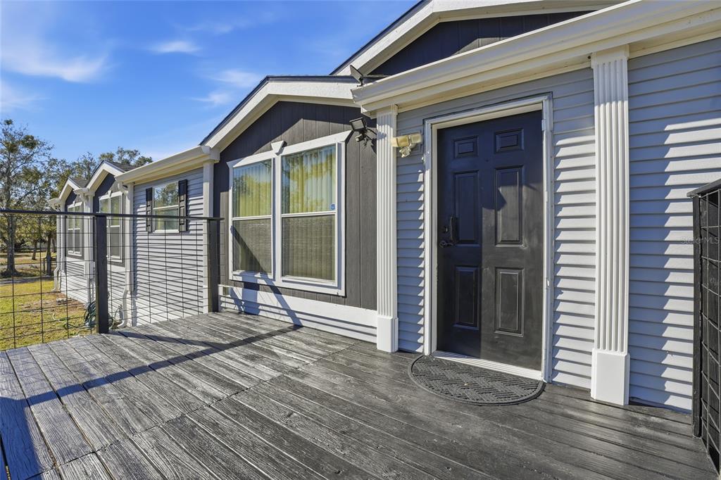 A wooden deck leads to a black front door on a light gray sided house — 3844 KAISER AVENUE, ST CLOUD, FL