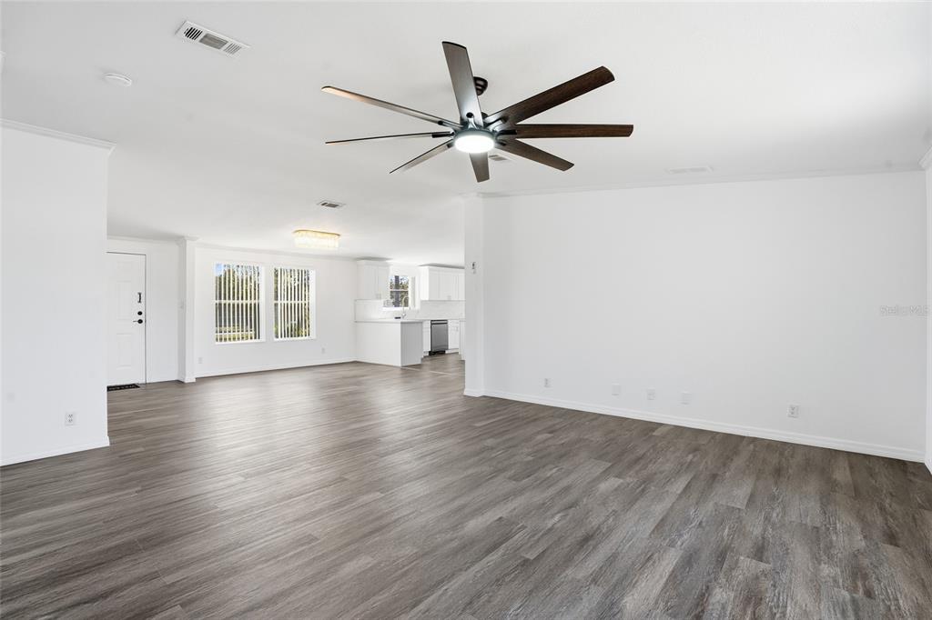 An open-concept living area features white walls, gray wood-look flooring, and a ceiling fan — 3844 KAISER AVENUE, ST CLOUD, FL