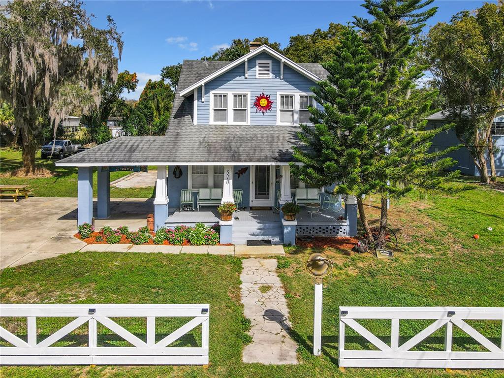 A blue two-story house with a front porch, white fence, and a large evergreen tree — 510 TIGHE AVENUE, SEFFNER, FL