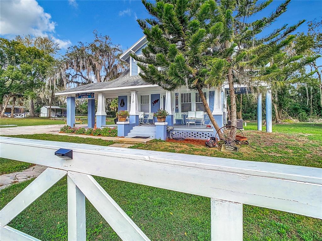 A blue two-story house with a wrap-around porch sits behind a white wooden fence — 510 TIGHE AVENUE, SEFFNER, FL