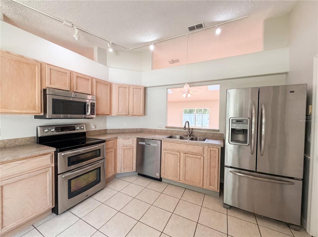 A kitchen with light wood cabinets, stainless steel appliances, and tile flooring — 1360 WILDBERRY LANE, DELTONA, FL