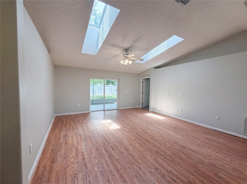 An empty living room features wood-look flooring, vaulted ceilings with two skylights, and sliding doors — 1360 WILDBERRY LANE, DELTONA, FL