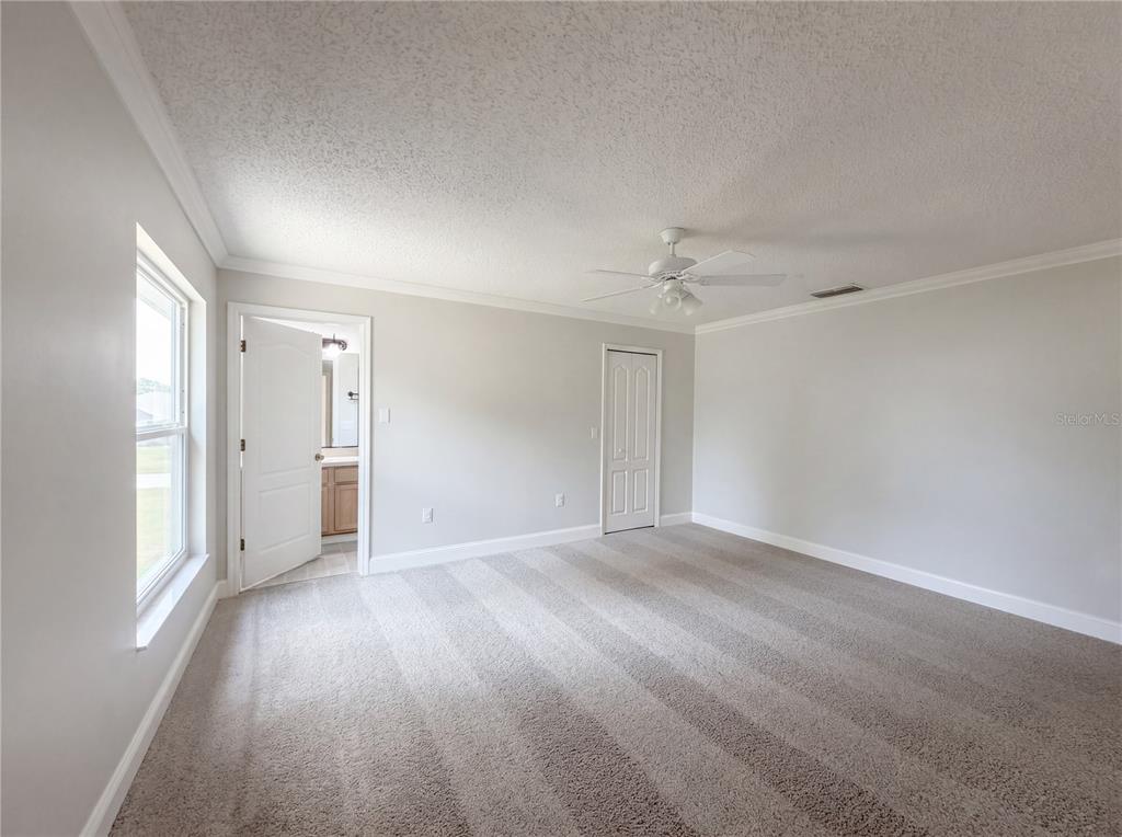 A bedroom with gray carpet, light walls, a ceiling fan, and an open bathroom door — 1360 WILDBERRY LANE, DELTONA, FL