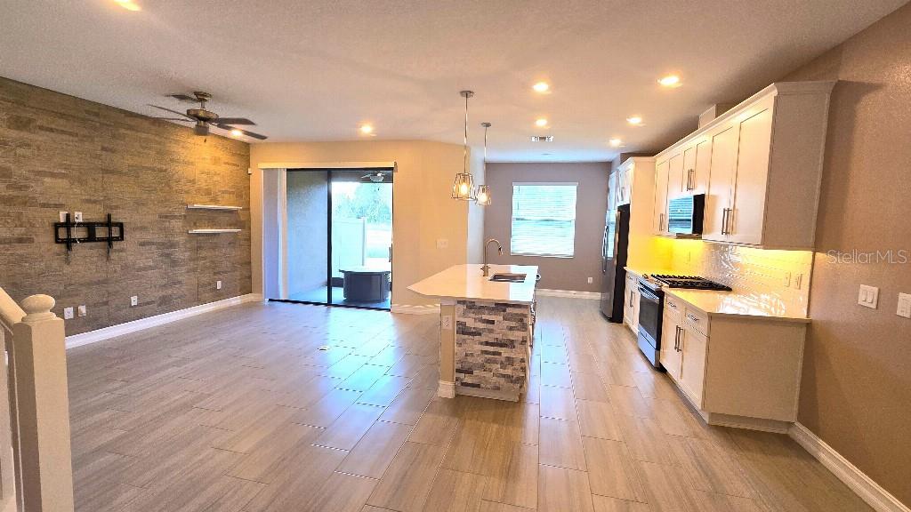 An open-concept kitchen and living area features tile flooring, a stone accent wall, and an island — 4887 ISOLA COURT, WESLEY CHAPEL, FL