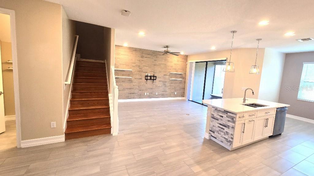 An open-concept living area features a wood-look tile floor, a stone accent wall, and stairs — 4887 ISOLA COURT, WESLEY CHAPEL, FL