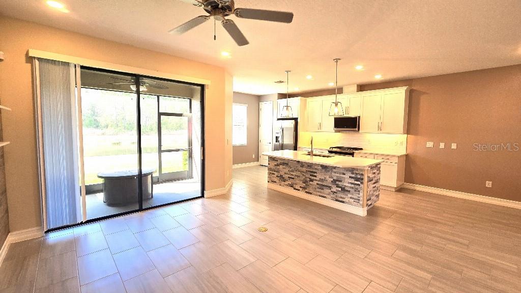 An open-concept kitchen and living area features a stone-faced island and sliding glass patio doors — 4887 ISOLA COURT, WESLEY CHAPEL, FL