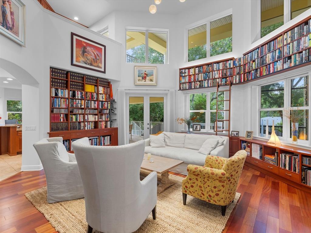 A living room features high ceilings, floor-to-ceiling bookshelves, a rolling ladder, and hardwood floors — 110 OCEAN WAY DRIVE, PONCE INLET, FL
