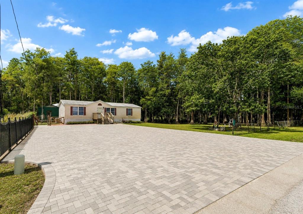 A single-story house sits behind a large paved driveway surrounded by trees — 17808 DOGWOOD DRIVE, LUTZ, FL