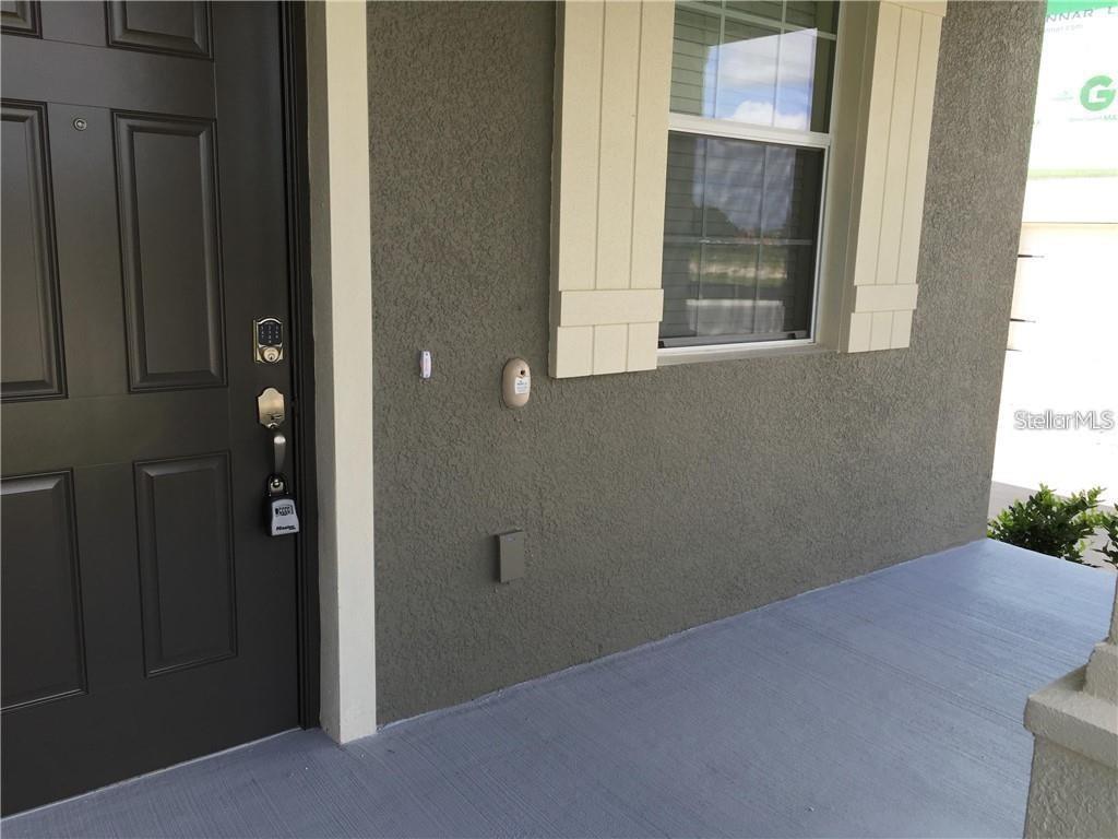 A dark front door with a keypad lock sits beside a window on a porch — 13048 GARRIDAN AVENUE, WINDERMERE, FL