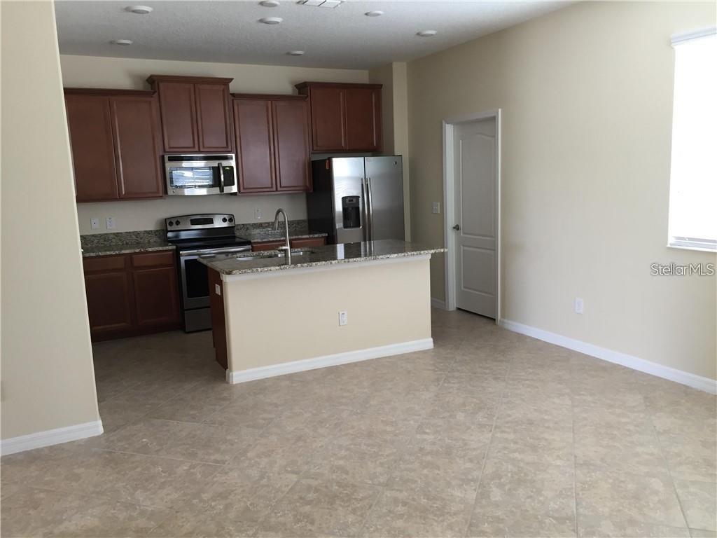 A kitchen features dark wood cabinets, stainless steel appliances, a granite island, and tile flooring — 13048 GARRIDAN AVENUE, WINDERMERE, FL