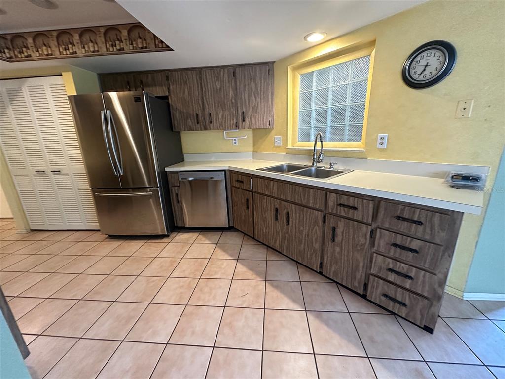 A kitchen features wood-grain cabinets, stainless steel appliances, a glass block window, and tiled flooring — 2361 ORANGESIDE ROAD, PALM HARBOR, FL