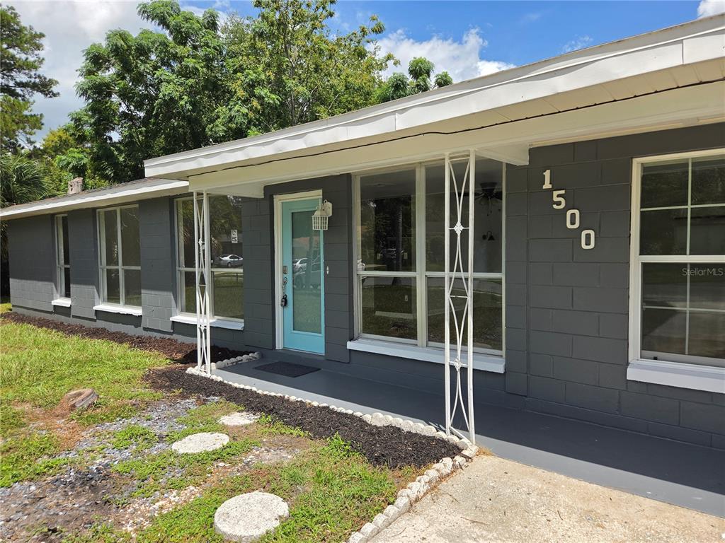A gray concrete block house features a light blue front door and white metal porch supports — 1500 CREST AVENUE, LEESBURG, FL