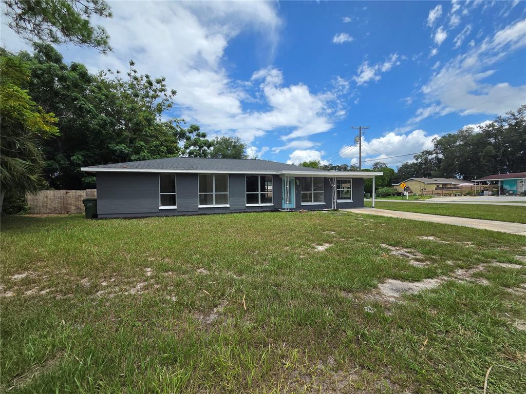 An empty living room features wood-look flooring, a ceiling fan, and a light blue front door — 1500 CREST AVENUE, LEESBURG, FL