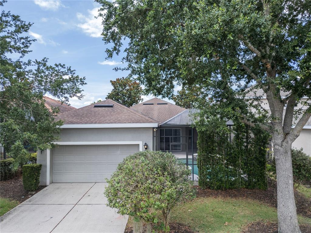 A single-story house with a two-car garage, a screened-in pool area, and mature trees — 7407 DEVEREAUX STREET, REUNION, FL