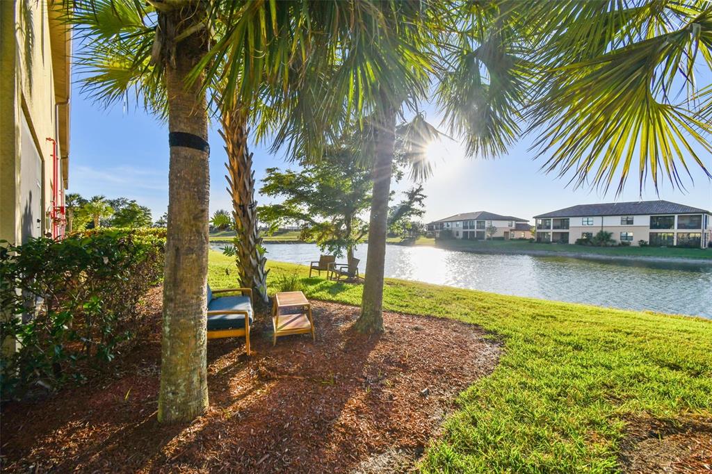 A patio area with chairs and a small table overlooks a lake and apartment buildings — 20252 LAGENTE CIRCLE, VENICE, FL