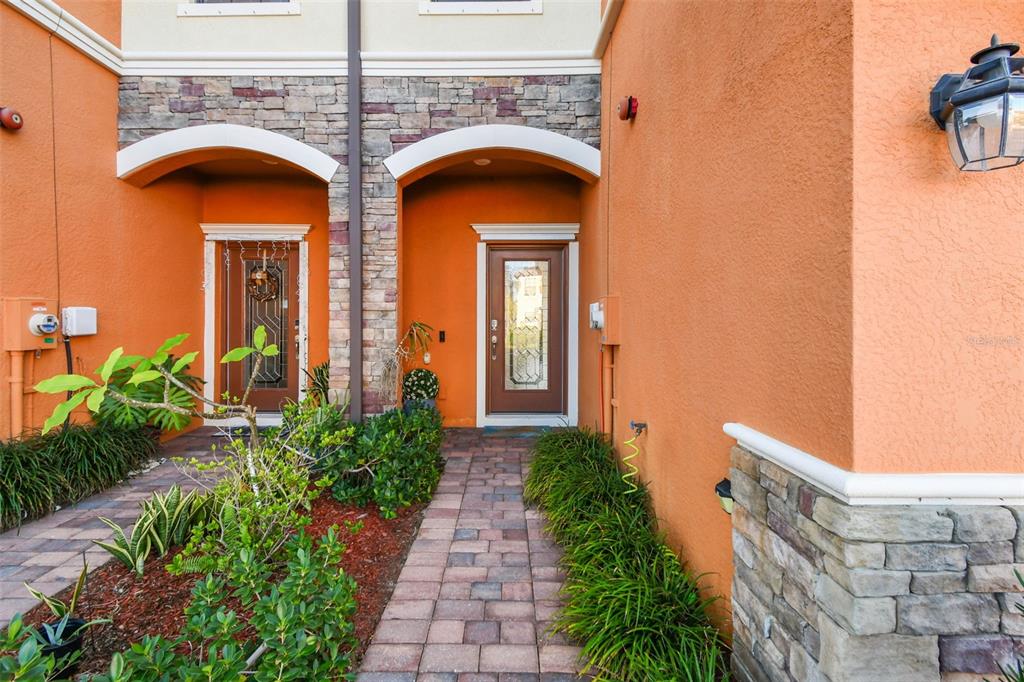 A paved walkway leads to two recessed front doors with stone accents and orange stucco walls — 20252 LAGENTE CIRCLE, VENICE, FL