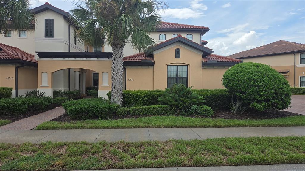A two-story stucco building with a tile roof, a palm tree, and manicured landscaping — 23556 AWABUKI DRIVE, VENICE, FL