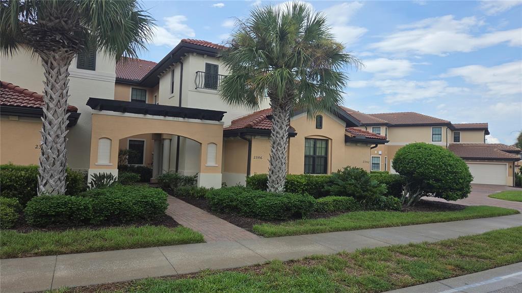 A two-story stucco building with a tile roof, palm trees, and a brick walkway — 23556 AWABUKI DRIVE, VENICE, FL