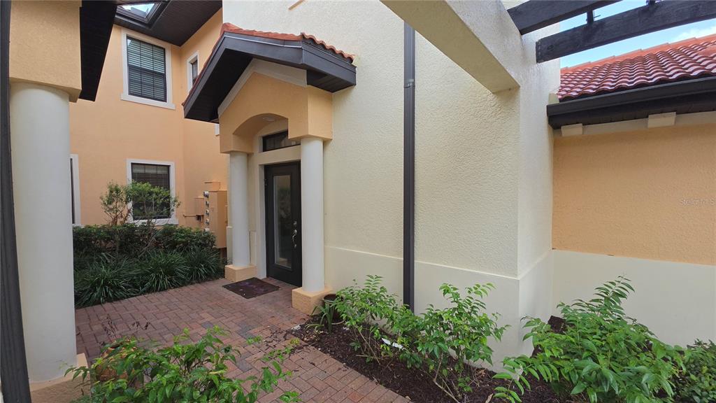 A brick walkway leads to the front entrance of a stucco home with white columns — 23556 AWABUKI DRIVE, VENICE, FL