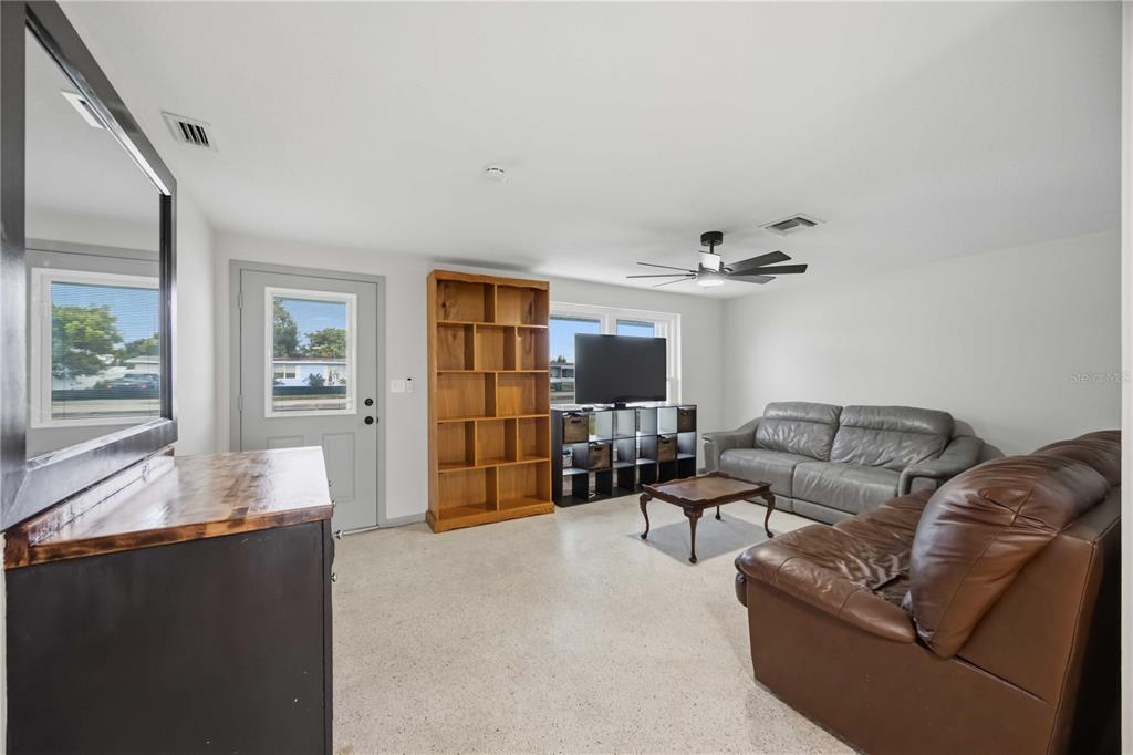A living room features a grey door, a wooden bookshelf, a television, and two leather sofas — 21298 MIDWAY BOULEVARD, PORT CHARLOTTE, FL