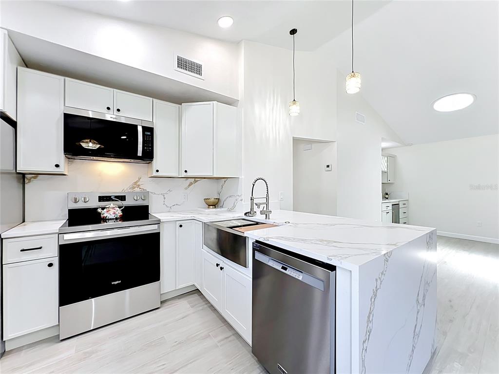 A modern kitchen features white cabinets, stainless steel appliances, and a marble-patterned countertop island — 1353 NELSON COURT, ROCKLEDGE, FL