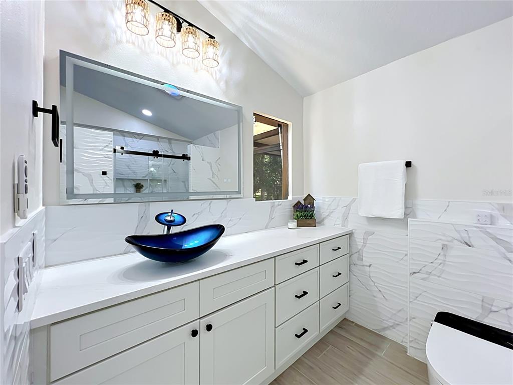 A bathroom features a blue glass vessel sink, white cabinetry, and marble-patterned wall tiles — 1353 NELSON COURT, ROCKLEDGE, FL