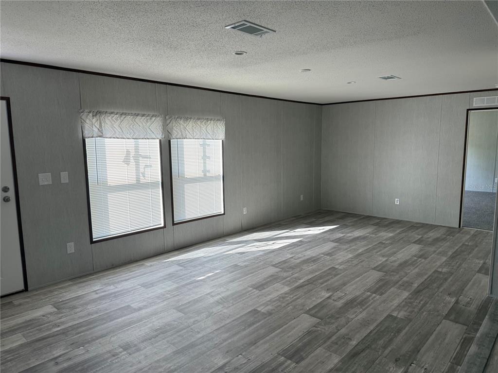 An empty living room features gray wood-look flooring, light gray walls, and two windows — 1561 POE ROAD, LAKE WALES, FL