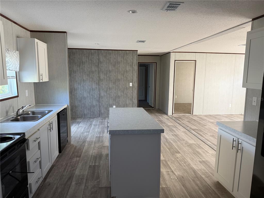 A kitchen with white cabinets, a central island, and wood-look flooring opens to a hallway — 1561 POE ROAD, LAKE WALES, FL