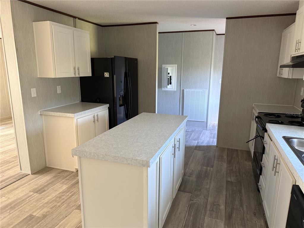 A kitchen features white cabinets, a central island, black appliances, and light wood-look flooring — 1561 POE ROAD, LAKE WALES, FL