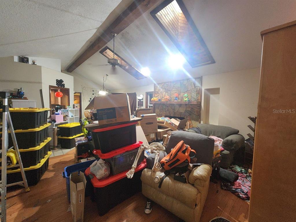 A cluttered living room features a vaulted ceiling with skylights, exposed beams, and a stone fireplace — 2407 SUMMER HOLLOW DRIVE, AUBURNDALE, FL