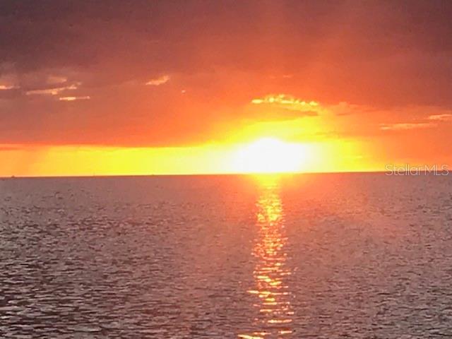 A vibrant sunset glows over the horizon above a calm, rippling body of water — SEBRING STREET, WEEKI WACHEE, FL