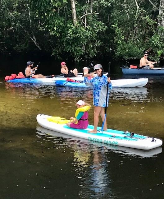 People paddleboard and kayak on a calm, tree-lined river — SEBRING STREET, WEEKI WACHEE, FL