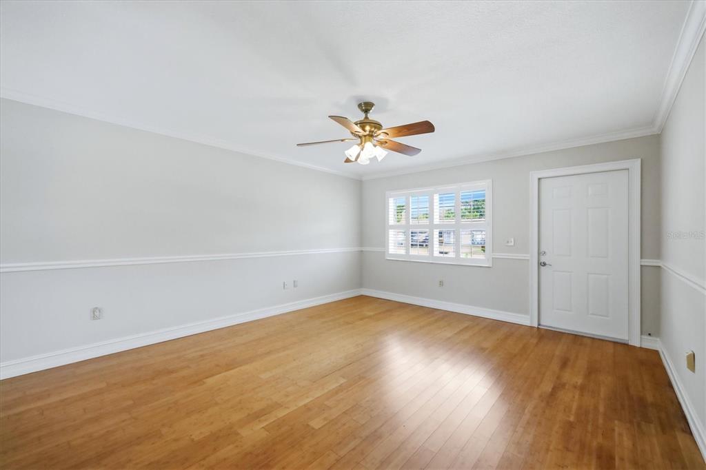 An empty room features light wood flooring, gray walls with white wainscoting, and a ceiling fan — 519 65TH AVENUE W, BRADENTON, FL