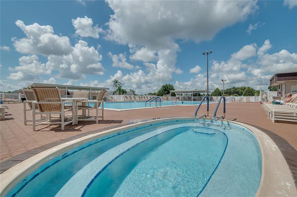A swimming pool and a hot tub are located on a paved patio under blue skies — 5970 CORMORANT COURT, LAKELAND, FL