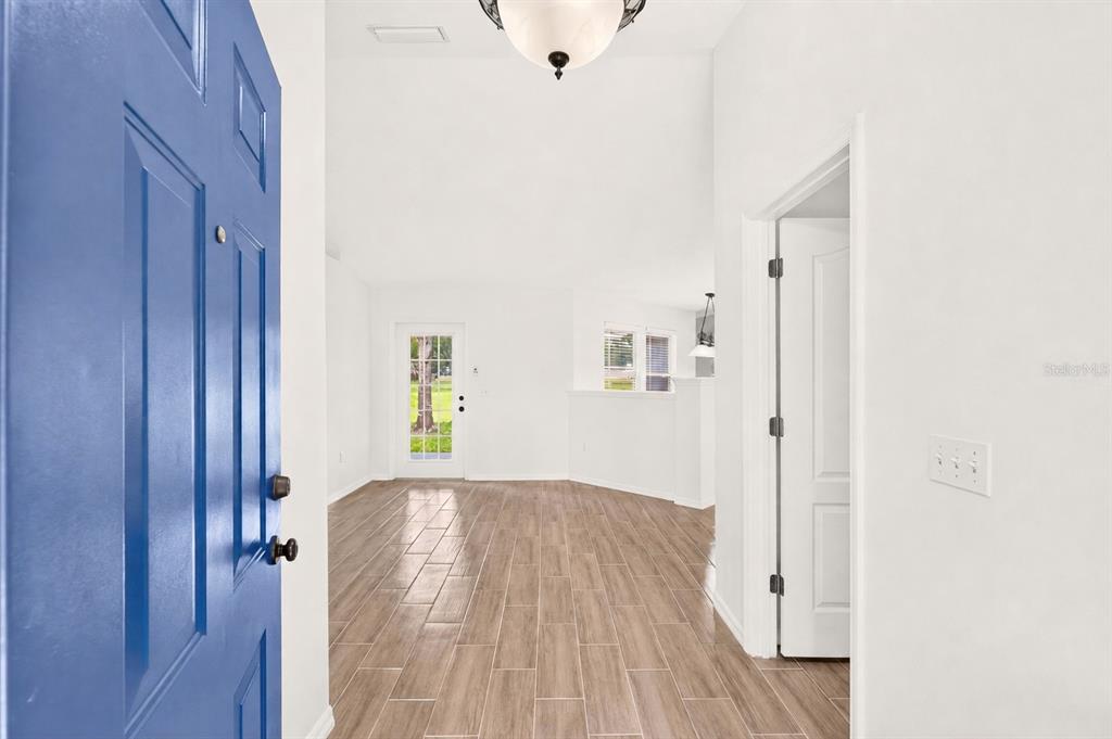 An entryway with a blue door opens into a bright room with wood-look tile floors — 8120 SW 52ND LANE, GAINESVILLE, FL