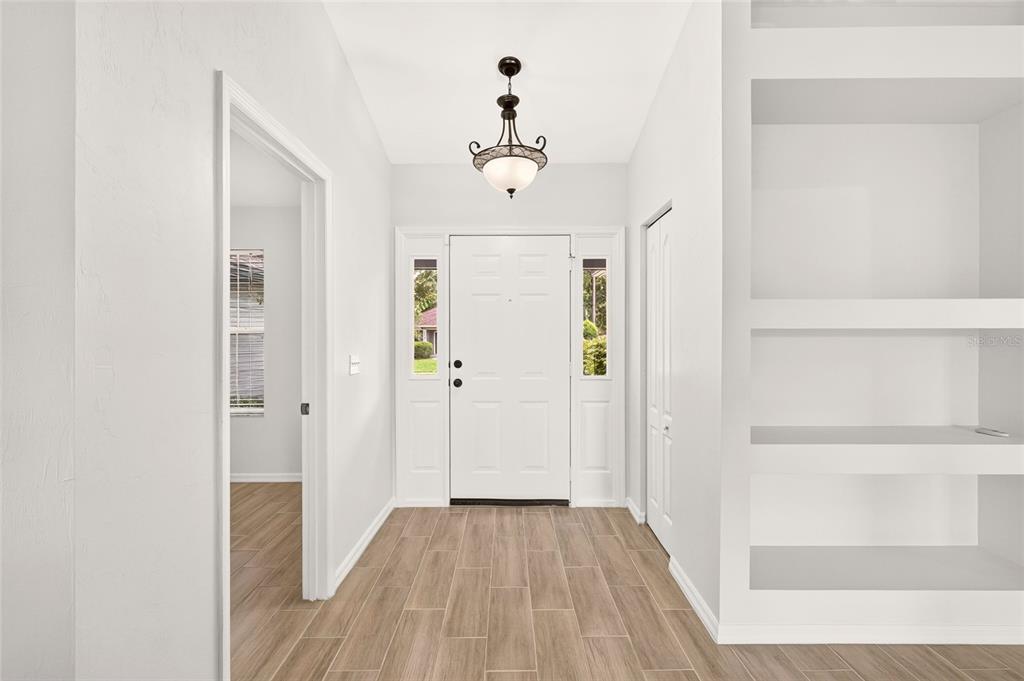 An entryway features a white front door, wood-look tile flooring, and built-in white shelving — 8120 SW 52ND LANE, GAINESVILLE, FL