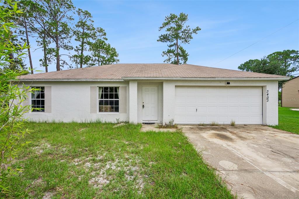 A single-story house with a white stucco exterior, a two-car garage, and a grassy yard — 3403 QUEEN PALM DRIVE, EDGEWATER, FL
