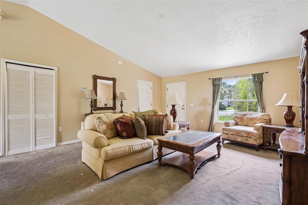A living room features beige walls, carpeted flooring, a sofa, an armchair, and a coffee table — 3403 QUEEN PALM DRIVE, EDGEWATER, FL