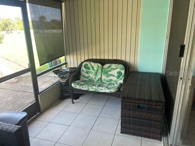 A screened-in porch features tiled flooring, a wicker loveseat with leaf-patterned cushions, and a storage chest — 5500 OCEAN SHORE BOULEVARD UNIT UT42, ORMOND BEACH, FL
