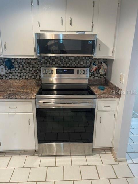 A kitchen features white cabinets, a stainless steel stove, a microwave, and a tiled backsplash — 5500 OCEAN SHORE BOULEVARD UNIT UT42, ORMOND BEACH, FL