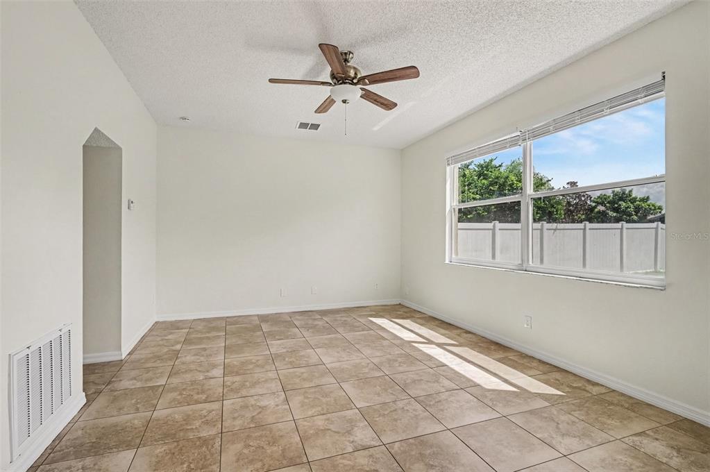 An empty room features beige tile flooring, white walls, a ceiling fan, and a large window — 14513 KAISER COURT, ORLANDO, FL
