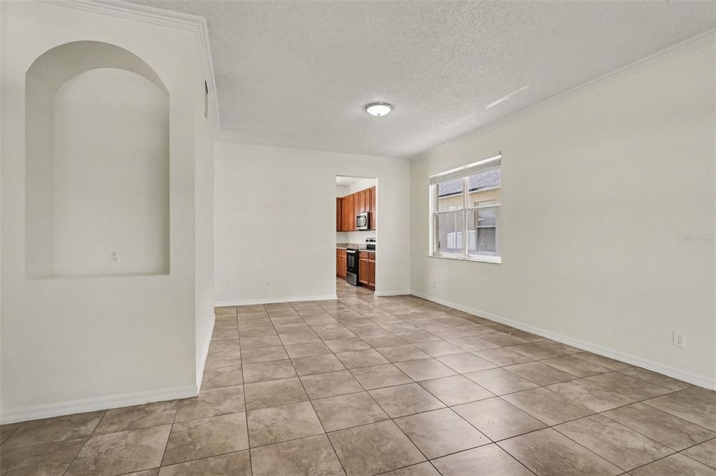 A room with light-colored walls, tiled flooring, an arched wall niche, and a kitchen view — 14513 KAISER COURT, ORLANDO, FL
