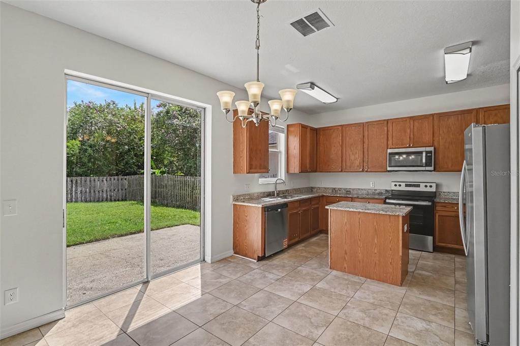 A kitchen with wood cabinets, granite countertops, stainless steel appliances, and a sliding glass door — 14513 KAISER COURT, ORLANDO, FL