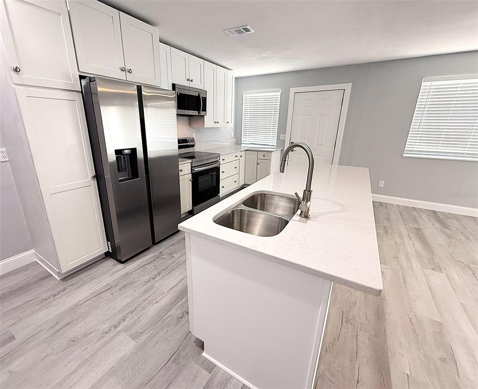 A kitchen features a central island with a sink, white cabinetry, and light wood flooring — 1231 ILLINOIS AVENUE UNIT 1, PALM HARBOR, FL