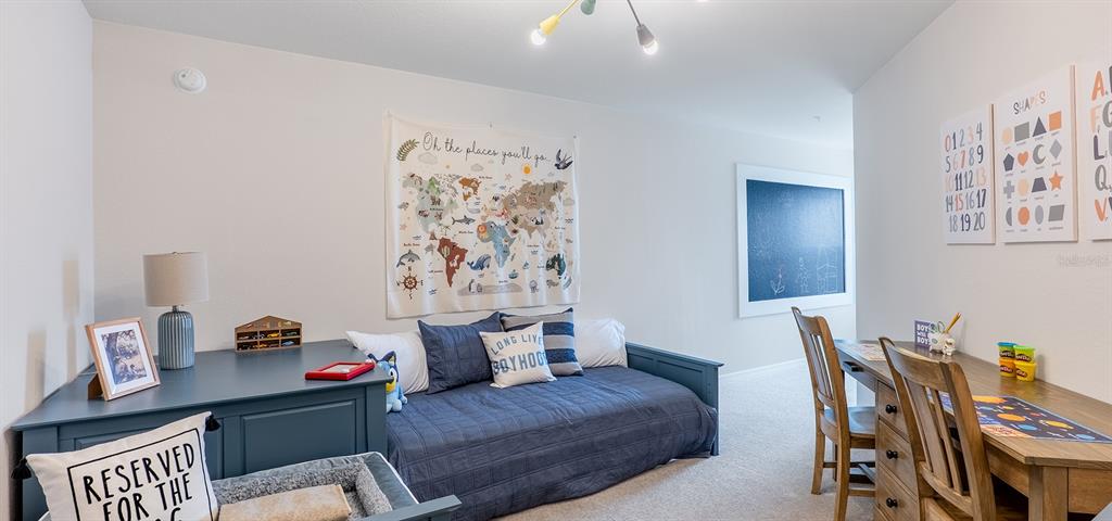 A bedroom features a blue daybed, a wooden desk with chairs, and wall-mounted educational posters — 398 CHESAPEAKE DRIVE, ST CLOUD, FL