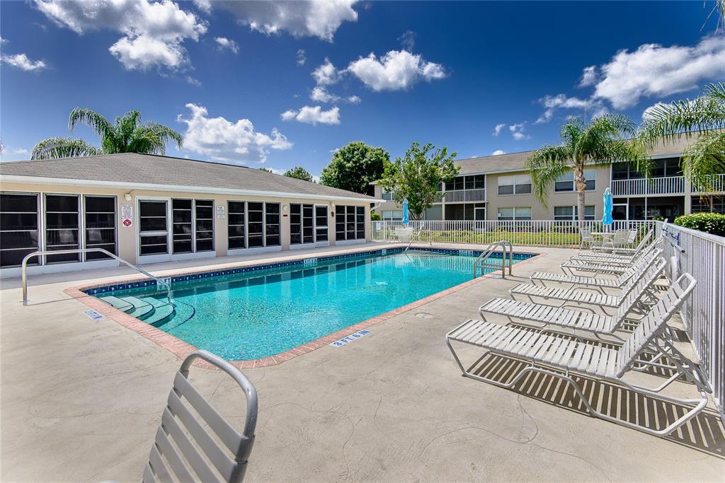 A rectangular swimming pool with lounge chairs sits in front of a multi-story apartment building — 11644 EGRET CIRCLE UNIT 1303, LAKE SUZY, FL