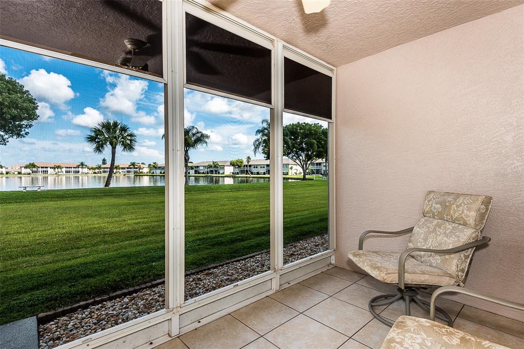 A screened-in patio with tile flooring overlooks a grassy lawn and a lake — 11644 EGRET CIRCLE UNIT 1303, LAKE SUZY, FL
