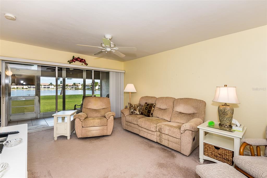 A living room features a beige sofa, a recliner, and sliding glass doors overlooking a lake — 11644 EGRET CIRCLE UNIT 1303, LAKE SUZY, FL